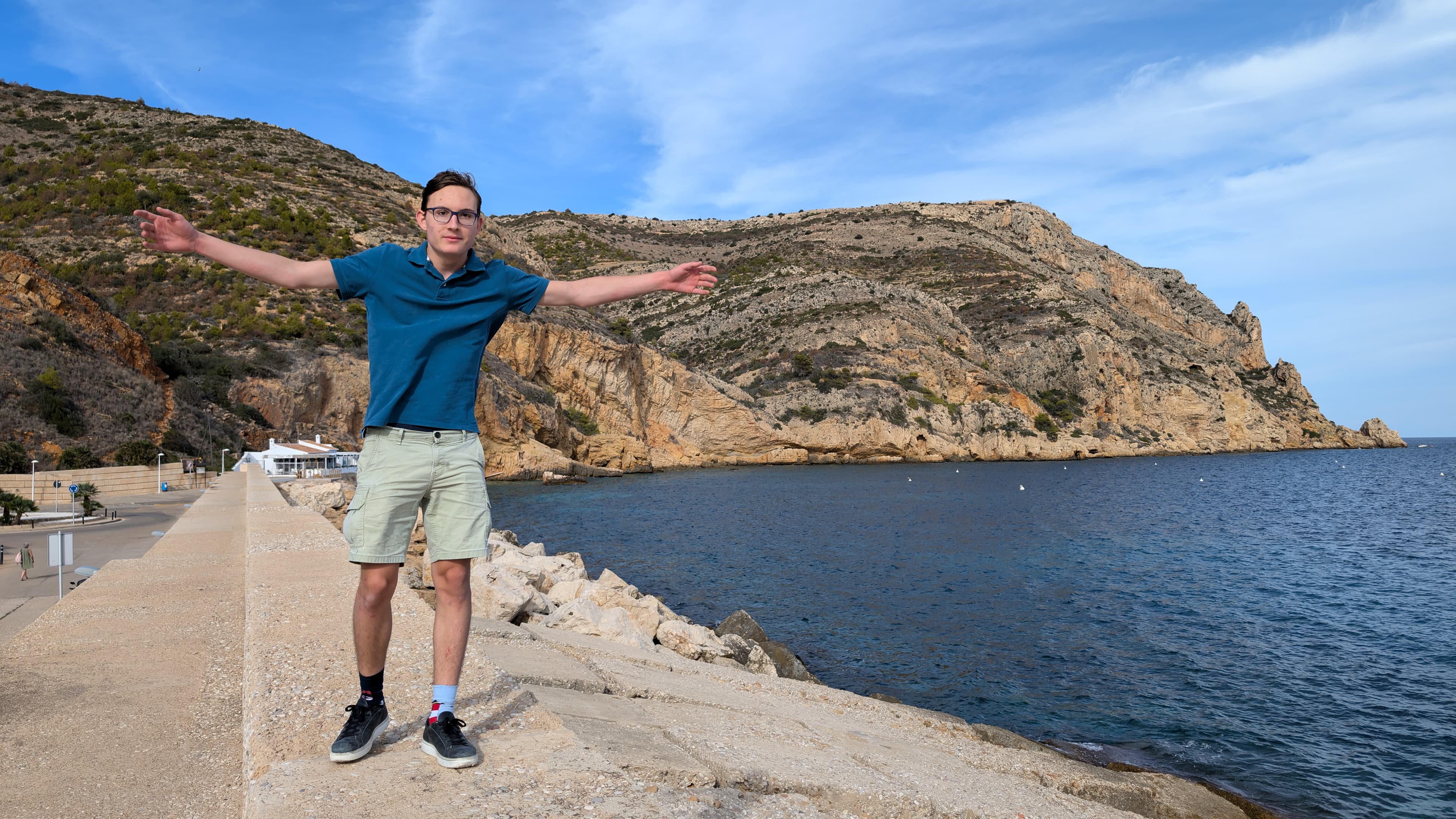 Frederik standing with outstretched arms beside the sea and rocky coastal cliffs